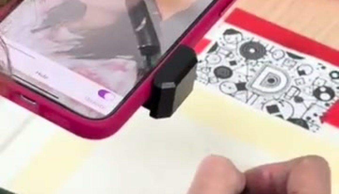 # Drawing with Da Vinci Eye In this screenshot from a Da Vinci Eye drawing tutorial, a person is using a smartphone mounted on a stand to project an image onto paper while drawing a portrait with a pencil, demonstrating how to use the app as a tracing aid for creating artwork.