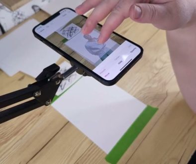 # Image Description A person is using the Da Vinci Eye app on their smartphone to trace or capture a reference image of a paintbrush, demonstrating how the digital tool helps artists study and replicate artistic subjects by photographing them through the app interface.