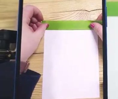 # Description A person is using an augmented reality app on their smartphone to practice drawing by holding a piece of white paper over a wooden surface with green tape, while the app displays "Anchor Not Detected" at the bottom.