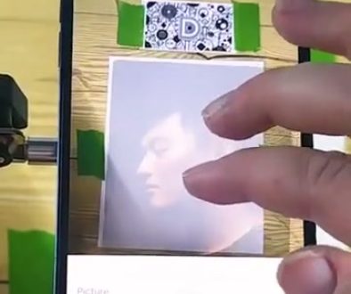 # Drawing App Interaction The person is using an augmented reality or drawing app on their iPhone to digitally sketch or manipulate an image of what appears to be an eye, with their finger actively engaged in the editing process on the screen.