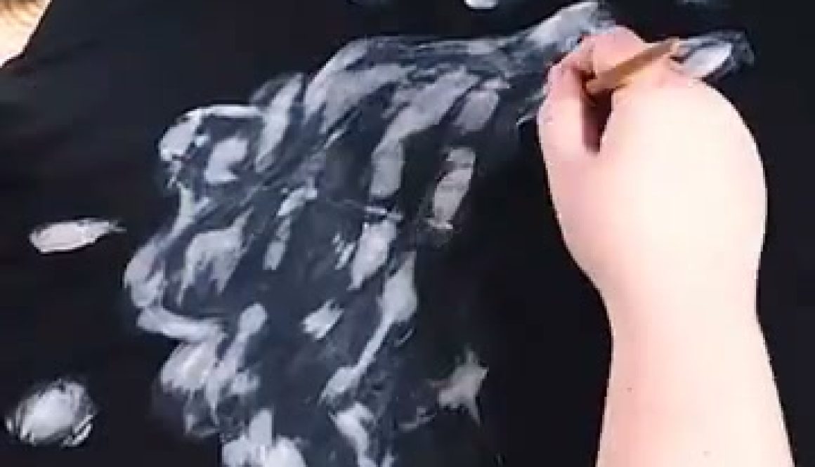 # Description A person is painting white highlights and details onto a black fabric using what appears to be white paint and a brush, creating a textured, cloudy effect as part of an art tutorial.
