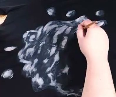 # Description A person is painting white highlights and details onto a black fabric using what appears to be white paint and a brush, creating a textured, cloudy effect as part of an art tutorial.