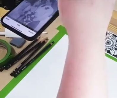 A person is drawing or tracing an image displayed on a smartphone onto paper using the Da Vinci Eye technique, which projects the phone's image to help with accurate sketching.