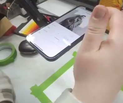 # Image Description A person is holding a smartphone displaying a reference image while sketching or drawing on a piece of paper below it, following along with a drawing tutorial.